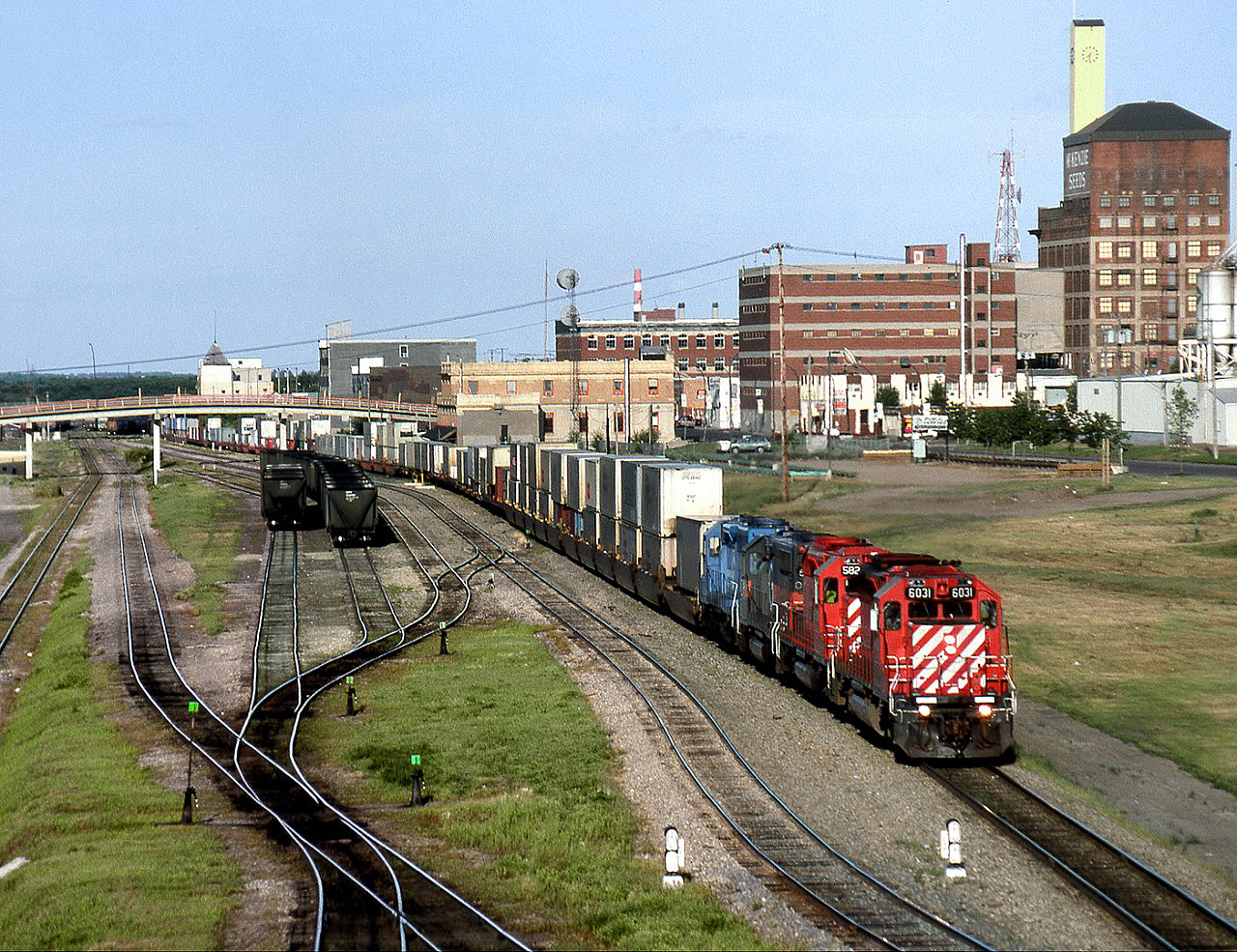 Westbound CP intermodal train 401 departs Brandon after changing crews at the Station, the yellow brick building below the bridge.