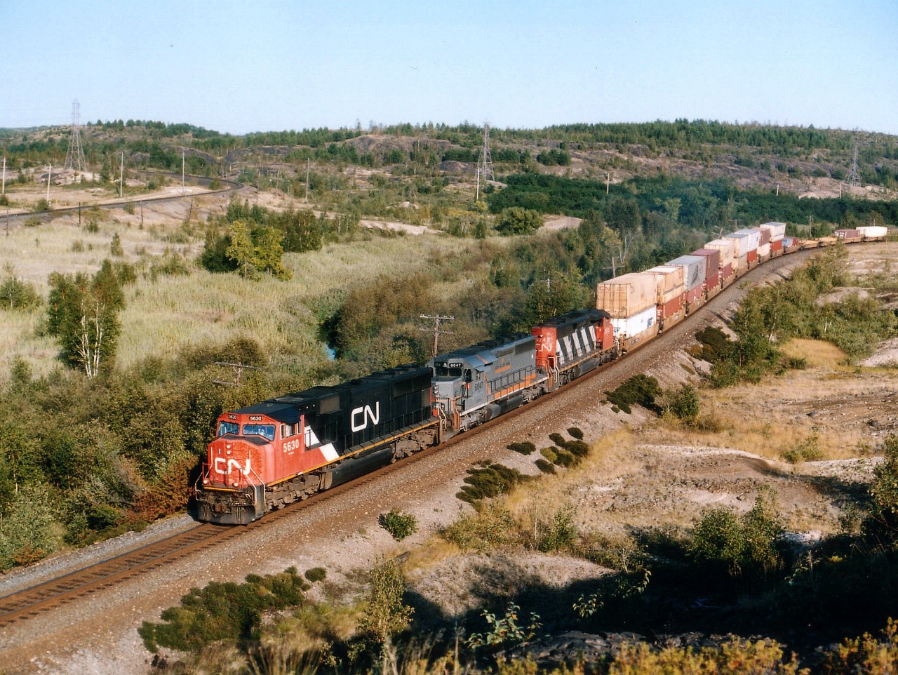 Westbound CN 5630, GCFX 6047 and CN 5242 approach the Coniston CN-CP diamond on a beautiful September afternoon, as seen from atop what I refer to as the 'slag heap', a huge pile of tailings from local mining. In the upper left can be seen the CP line from North Bay. The GCFX, an SD40-3, is from Connell Leasing; in its former life it toiled as SD40 CN 5219.