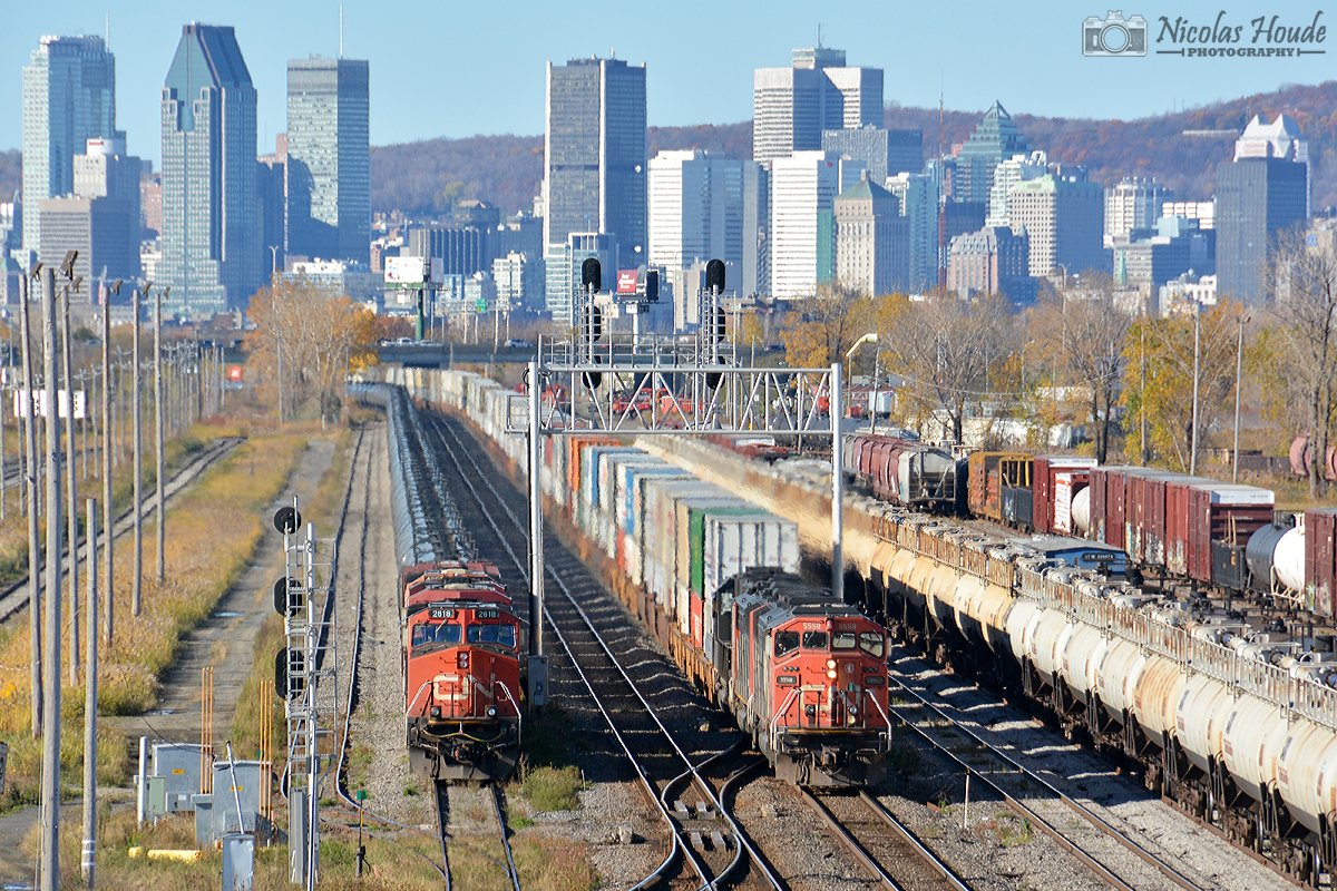 CN Q12031 01 pass on north track on the CN Saint-Hyacinthe Subdivision beside the CN U71091 01. In background, you can see the Montreal skyline.