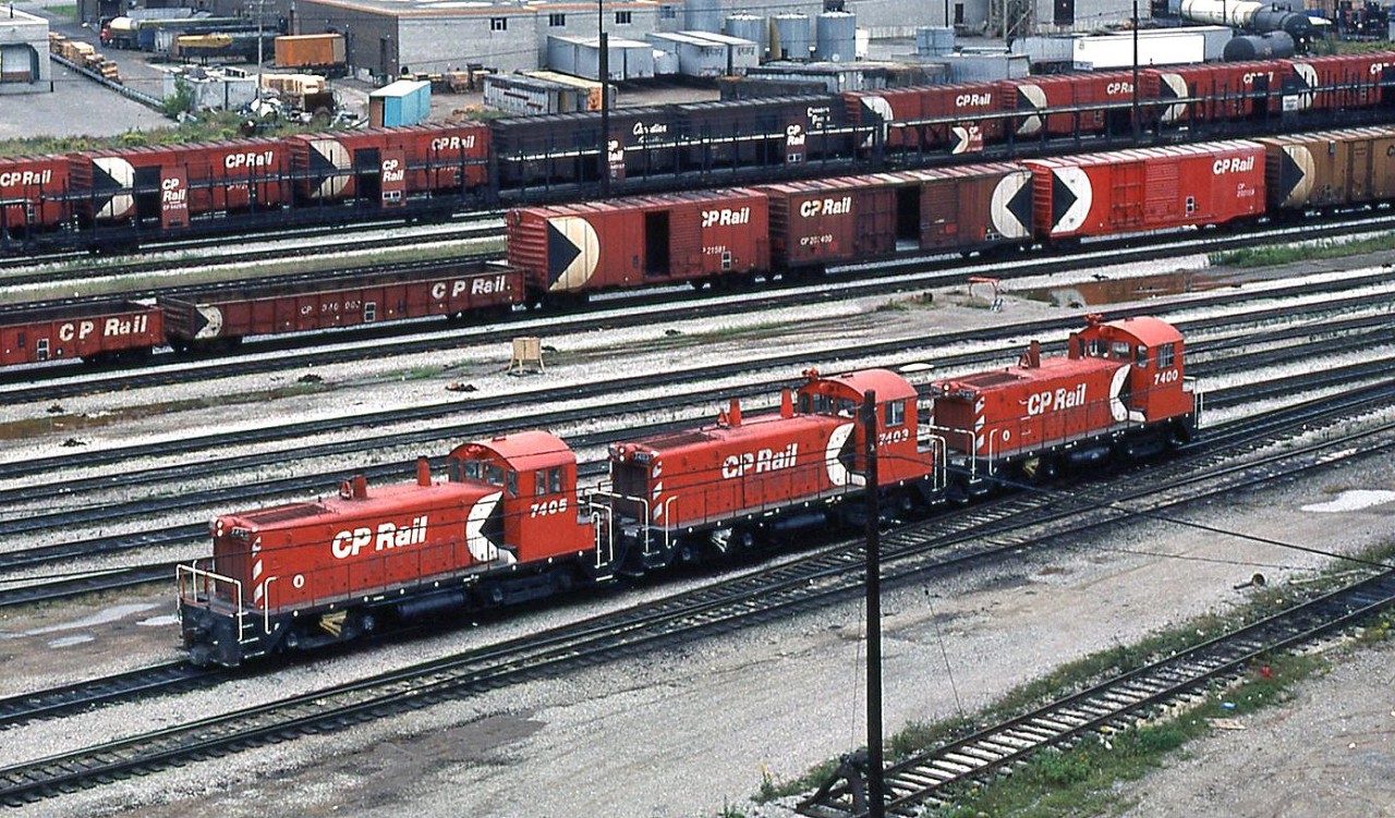 In the 60's, 70's and early 80's prior to the invasion of rebuilt GP7 and GP9's, hump operations at Canadian Pacific's large Toronto Yard in Agincourt (a neighborhood in Scarborough, which was a borough in Toronto) were handled with pairs and later trios of GMD SW9's. Three are shown here near the General Yard Office: CP 7405, 7403 and 7400, between humping duties.  CP only ordered six of the 1200 horsepower SW9 switchers numbered 7400-7405 (later buying 72 of the upgraded SW1200RS road switcher model), and they remained the largest of CP's switcher fleet compared to other 660, 800, 900 and 1000 hp units. Initially the six were used in switching service out west, but migrated to the east for use at the hump in the newly opened Toronto Yard in the 60's (three SW1200RS units would later be used on the hump with them). Units 7400-7403 were equipped with cab signal gear and slow speed hump control (note the repositioned horns and signal gear installed on the cabs of 7400 & 7403), while units 7404 and 7405 were just equipped with rear MU to be operated trail-only. The engineer would operate the set out of the rearmost cab, in this case, unit 7400. At the time, all 3 here are wearing the later version of the multimark livery with the logo on the hood instead of the cab, and all have been modernized with dual-sealed beam headlights and full side handrails (also note the additional numberboards they received). They would be rebuilt as 1200 series units in two or three years for general switching duties, and 3-packs of more powerful rebuilt GP7u/GP9u's would take over hump duties here.  In the background is a whole bunch of classic CP Rail 1970's rolling stock: action red 52' mill gondolas, red 40' boxcars, 50' double door boxcars (that were actually rebuilt by CP from 40' single door boxes), an insulated-heated yellow 40' box, open autoracks, and a pair of 40' boxes in the older script and stacked lettering schemes. A few customer sidings, long gone today, can be seen in the background at the south end of the yard along Nugget Avenue.  For further reading on Toronto Yard, there is an excellent writeup on Ray Kennedy's Old Time Trains website here.