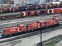 In the 60's, 70's and early 80's prior to the invasion of rebuilt GP7 and GP9's, hump operations at Canadian Pacific's large Toronto Yard in Agincourt (a neighborhood in Scarborough, which was a borough in Toronto) were handled with pairs and later trios of GMD SW9's. Three are shown here near the General Yard Office: CP 7405, 7403 and 7400, between humping duties. <br><br> CP only ordered six of the 1200 horsepower SW9 switchers numbered 7400-7405 (later buying 72 of the upgraded SW1200RS road switcher model), and they remained the largest of CP's switcher fleet compared to other 660, 800, 900 and 1000 hp units. Initially the six were used in switching service out west, but migrated to the east for use at the hump in the newly opened Toronto Yard in the 60's (three SW1200RS units would later be used on the hump with them). Units 7400-7403 were equipped with cab signal gear and slow speed hump control (note the repositioned horns and signal gear installed on the cabs of 7400 & 7403), while units 7404 and 7405 were just equipped with rear MU to be operated trail-only. The engineer would operate the set out of the rearmost cab, in this case, unit 7400. At the time, all 3 here are wearing the later version of the multimark livery with the logo on the hood instead of the cab, and all have been modernized with dual-sealed beam headlights and full side handrails (also note the additional numberboards they received). They would be rebuilt as 1200 series units in two or three years for general switching duties, and 3-packs of more powerful rebuilt GP7u/GP9u's would take over hump duties here. <br><br> In the background is a whole bunch of classic CP Rail 1970's rolling stock: action red 52' mill gondolas, red 40' boxcars, 50' double door boxcars (that were actually rebuilt by CP from 40' single door boxes), an insulated-heated yellow 40' box, open autoracks, and a pair of 40' boxes in the older script and stacked lettering schemes. A few customer sidings, long gone today, can be seen in the background at the south end of the yard along Nugget Avenue. <br><br> <i>For further reading on Toronto Yard, there is an excellent writeup on Ray Kennedy's Old Time Trains website <b><a href="http://www.trainweb.org/oldtimetrains/CPR_Toronto_Yard/History_1.htm">here</a></b>.</i>