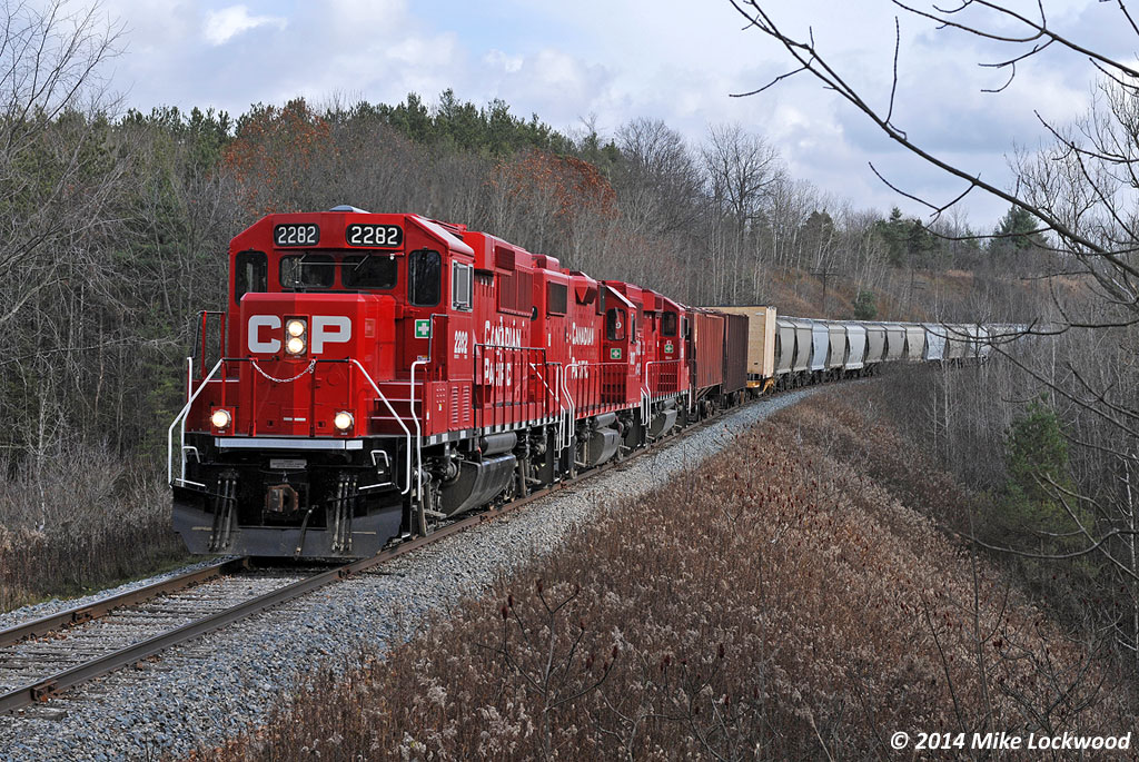 Ambling their way west across the top of the Oak Ridges moraine, CP 2282, 3027, and 2259 lead T07's train, including a 400,000lb wind turbine generator load, through a spot I find most appealing near Raglan, Ontario. It's hard to tell from the photo, but the power is atop a tall, albeit short, fill across a small dell which opens on the north (left) into a bucolic farm field. I imagine this would have been the location of a temporary trestle during the Ontario & Quebec Railway's construction... the deep cut the train is emerging from would have supplied the material to make it's existence short indeed. 1118hrs.