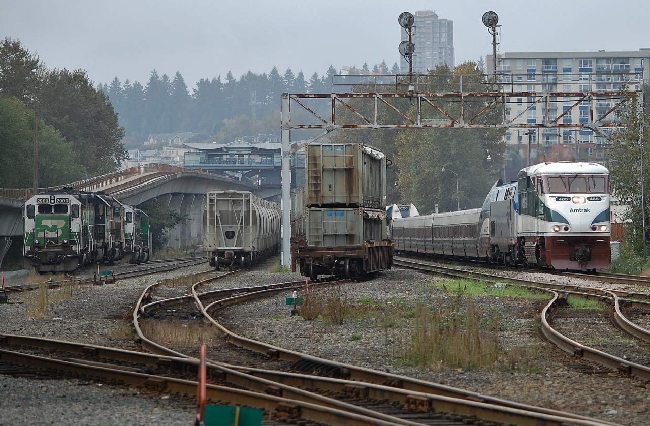 The morning Amtrak "Cascades" is passing through New Westminster and headed for Vancouver behind AMTK nos.465 & 48. On the left can be seen Sapperton Sky Train station and a line of BNSF power units.