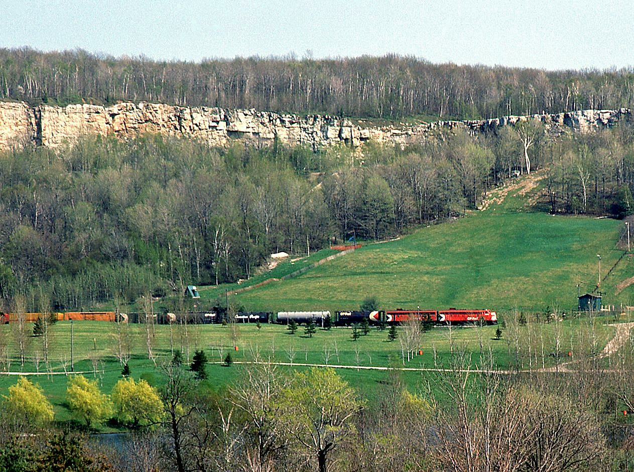 Classic A-B first generation diesel power in freight service: 25-year old unrebuilt CP FP7 4031 and F7B 4433, in charge of a westbound extra, are stalled climbing the grade up the Niagara Escarpment near Mile 35 of the Galt Subdivision. In the background, the Kelso Conservation Area ski hill looms apparent, with the conservation area's pond in the foreground, and The King's Highway 401 in front of the photographer but not visible.Eventually the train would get on the move again, captured here rolling through Campbellville near Guelph Junction.