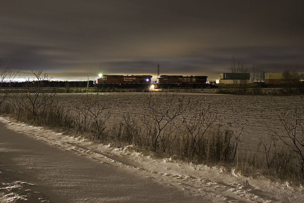 Not exactly a common sight. A high priority CP intermodal freight stopping practically in the middle of nowhere. CP 101 has come to a stop just short of Side Road 25. The reason? I am unsure myself, as my radio is broken. Scanning the tracks for trains as I do sometimes, I noticed an approaching northbound that appeared to be moving rather slow. I decided to head up to Side 30 in hopes of seeing it there. By the time I was there, I noticed the headlights of 101 had still not passed the signal just north of 6th Line. I returned to Side Road 25, and as I was coming up the crossing, the train was stopped just short of it, and the crossing lights  deactivated right as I got there. So an emergency brake application was out of the question. Crew running out of hours, maybe?... Despite being close to Barrie, this seems like a random location to leave a train, on single track, and Baxter siding being less than 5 miles south of here. Whatever the reason, I decided to take advantage of this opportunity by taking a long exposure of 101. Light pollution is from Barrie's south end.