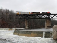 With a break from the earlier snow flurries CN 5291 and CN 5519 lead a mixed freight east across The Grand River viaduct at Paris. In the foreground is Penman's Dam.