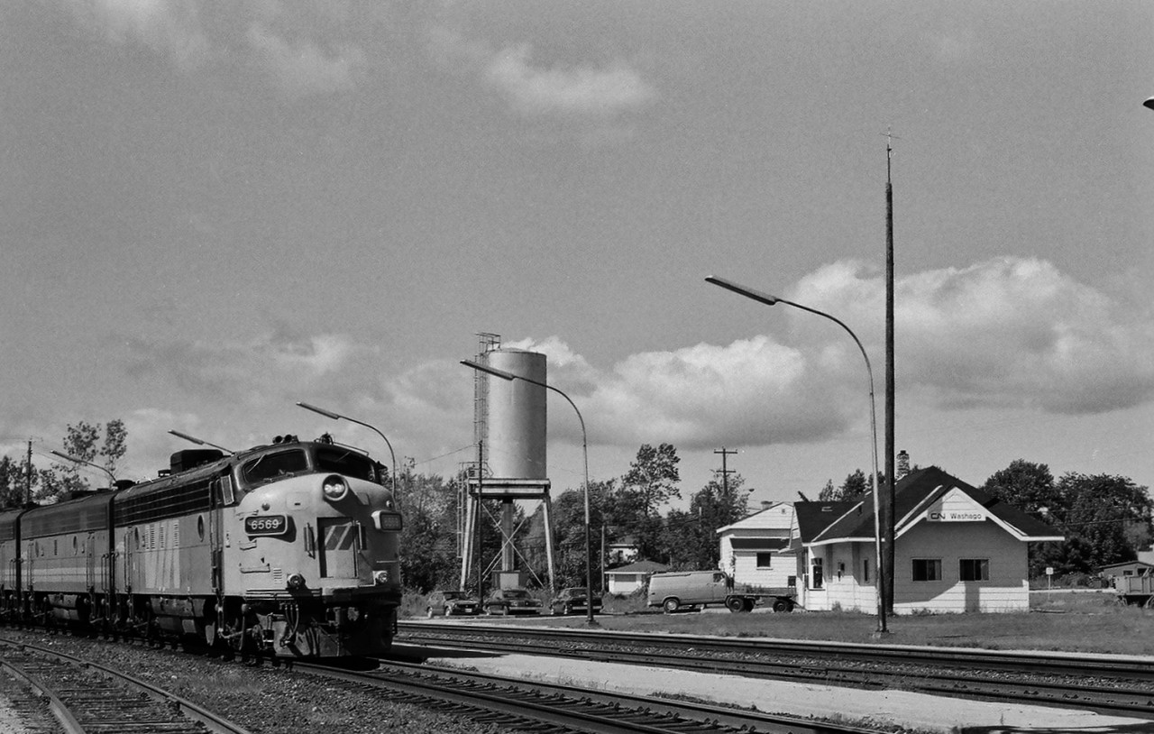 One of my favourite places.


Three roads. 


Eight trains on Sunday, 


seven on Friday, 


six on each of Monday to Thursday,  


five on Saturday


and was just the passenger service  circa 1976 through 1989.


In addition to the usual CN wide cab GP40's, freight included the occasional ONR unit  train (ore pellets for Dofasco).


This is the second of two images. The first :
 

    Via #9  


...Algonquin Park (Via 15501) just cleared the Quetton Street crossing as the twelve car Via # 9 powered by 6507 – 6627- 6761 (FP9A – F9B – FPA4 ) departed CN Washago on time 15:30 August 5,1985.


.. Unexpectedly the crossing gates remained in the down position, then Via #10  with 6569 rolls into Washago  one hour twenty minutes off schedule. 


August 5, 1985 negative by S.Danko


What's Interesting: 


The ex CP Rail passenger equipment showed up 1979 when Via consolidated the transcontinental train into one daily.


 #10 to service Orillia, Barrie, Newmarket and the St. Clair Avenue CN Newmarket Subdivision stations with the new day light service  commencing June 1 1985, the first day light Via service on the Newmarket since 1980.   


 Via FP7A 6569 survives today as West Coast Railway #4069.  The 6569 is ex Via 1425 exx Via 4069 exxx CP 4069 exxxx CP 1425 exxxxx CP 4069 (built GMDD October 1954).


The Washago Station remains on the old right of way alignment that was changed in the early 1960's when the highway #11 overpass was constructed.


The water tower was in town water service.


sdfourty.