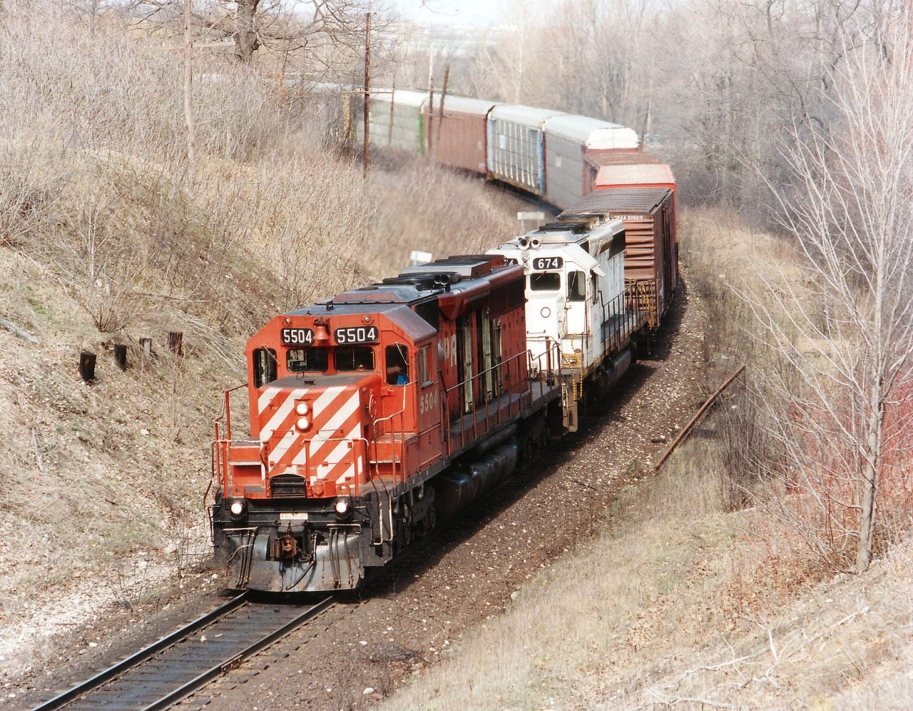 A daily occurrence, but with a variety of power, London Pickup #923 swings westward in the mid-afternoon toward home as seen in this view off the side of the cut at Orrs Lake. Location is just west of the big Grand River Bridge in Cambridge. Straight SD40 #5504 leads an SD40-2 in Kansas City Southern white; this unit one of 7 leased (670-676) from Helm in early 1992, resulting in CP purchasing them outright by the years' end. The 674 was slotted into the CP roster as 5419; it was retired in 2006. Orrs Lake namesign can be seen just over the 674's body. The area is rather overgrown these days.