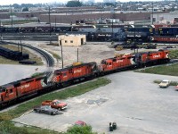CP Rail SD40-2 5660, C424 4201, GP35 5007 and RS23 8026 head around the wye in CP's sprawling Toronto Yard as viewed from near the hump crest.
<br><br>
Likely a light power move to or from the shops, by this time the first three units were all still DRF units or "Diesel Road Freight", classified as such by CP for mainline freight service. 5660 would remain a DRF unit, but 4201 and 5007 would be rebuild and reclassified as road switchers ("DRS" class) a few months later as part of CP's 10 Year Rebuilt Program. 8026 is 1000hp MLW RS23 CP knew as a Branch Line Unit (BLU, formally a "DRS-10" in this case), and like the SW1200RS Pups, the RS23 units acquired a nickname of their own: "Rockets."
<br><br>
There's a lot present in this photo. In the background are the industrial buildings and factories located off Middlefield Road, and beyond that the residential neighbourhoods west of McCowan. Freight cars present in the yard include green CP 40' newsprint boxcars, C&O "Chessie System" double door boxcars, some short N&W covered hoppers, a cut of CP script cylindrical hoppers coupled to an action red gondola, and some Conrail open hoppers to the left. Also not to be overlooked are the assortment of now-vintage automobiles in the parking lot, including a red-orange Chevy pickup and what looks to be an AMC Gremlin hiding behind the bushes.
<br><br>
CP's Toronto Yard, located in the Agincourt neighbourhood of Scarborough in Toronto, was opened in April 1964 due to the need for larger yard facilities than Lambton and West Toronto yards. It continues serving freight operations today, albeit without an operational hump and with some of the hump classification tracks being removed.