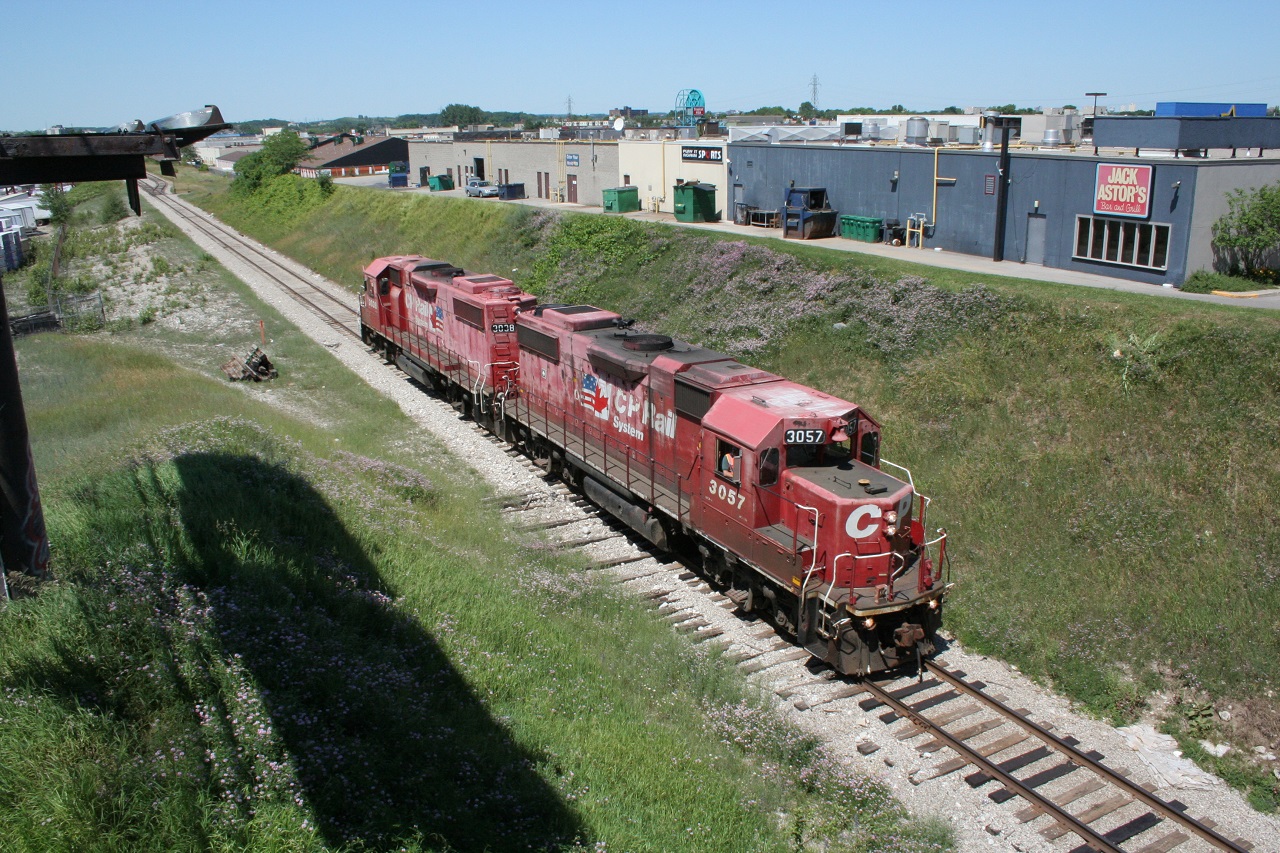 CP 3057 and CP 3038 in the old "dual flag" paint scheme head towards Cambridge as light power in the summer of 2008. They are about to duck under the Wilson Avenue overpass and are paralleling the busy Fairway Road in the south part of Kitchener. Note how faded the paint is on these locomotives - the red has become pink! Contrast this with the vibrant red paint on the new CP GP20C-ECOs that are currently dominating this level of power.