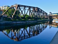 VIA 37 has VIA 6405 is leading as it crosses over the Lachine Canal. It is passing a CN swing bridge which is no longer in use and is locked in place.