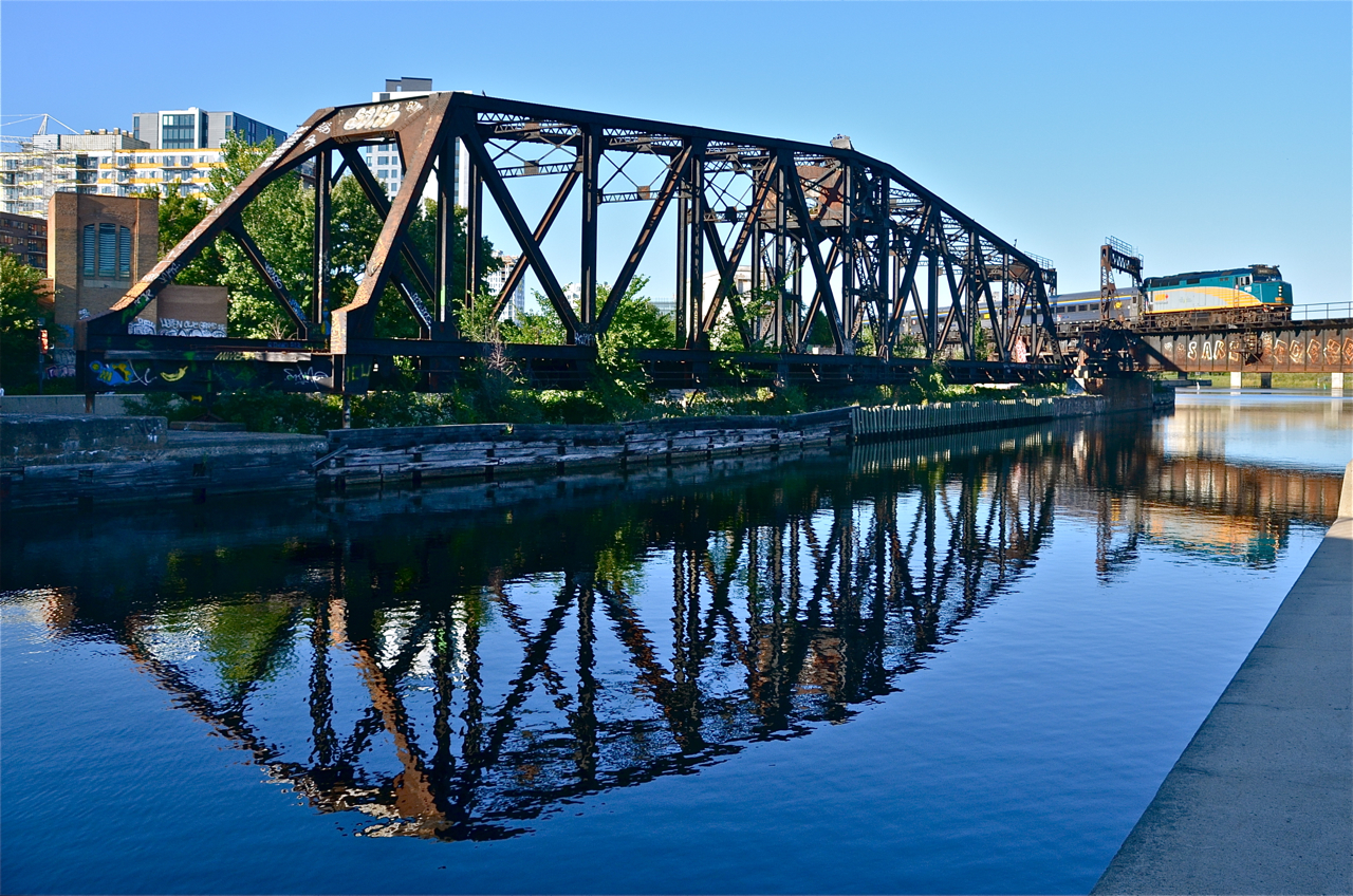 VIA 37 has VIA 6405 is leading as it crosses over the Lachine Canal. It is passing a CN swing bridge which is no longer in use and is locked in place.