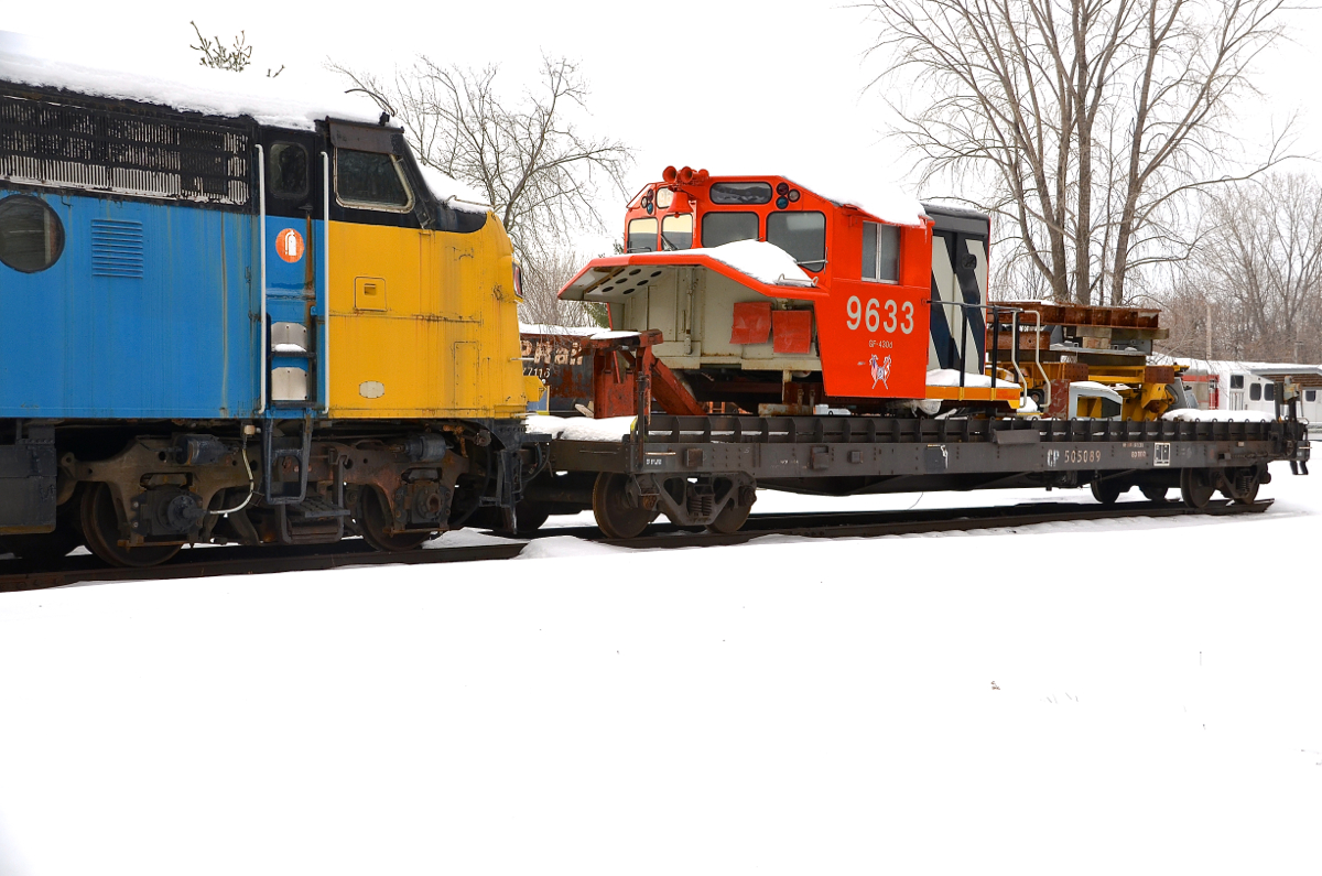 Snow-covered locomotive simulator. The locomotive simulator 'CN 9633' (previously for sale, current status unknown) is back at Exporail, here on a flat car which is coupled to VIA 6309, both snow-covered.