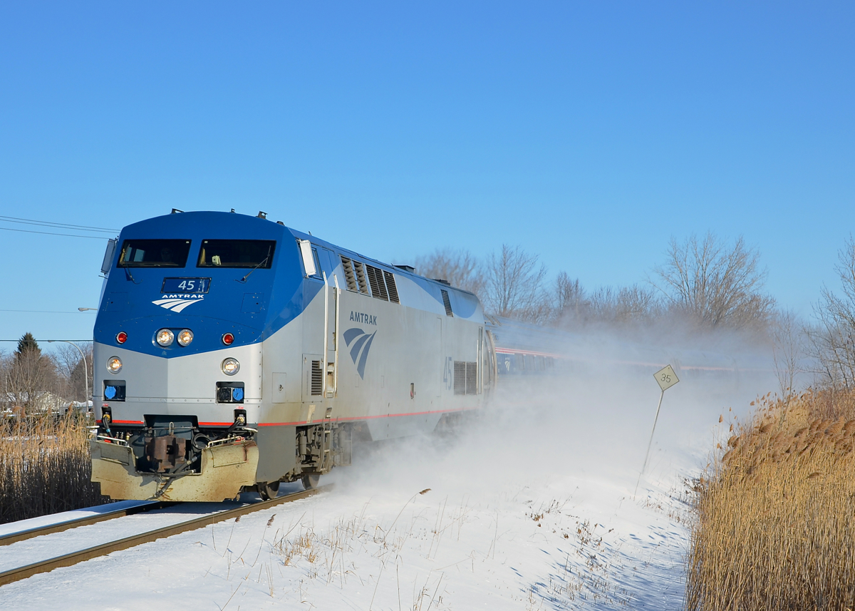 The amfleet cars trailing AMTK 45 on the southbound Adirondack are partially obscured by the snow that it's kicking up as it approaches a grade crossing in Brossard, Qc on a very cold morning.