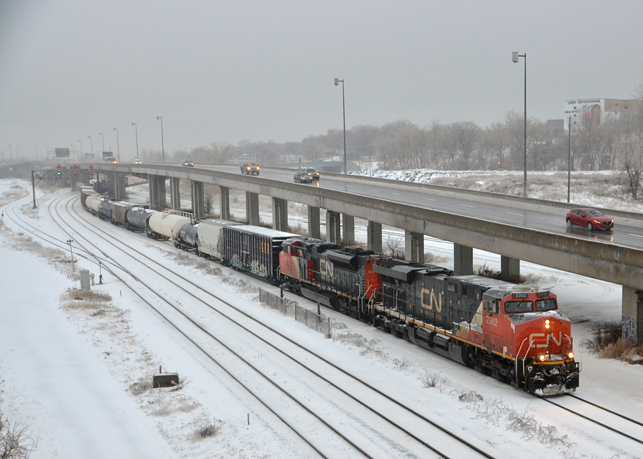 CN X394 for Richmond, Qc heads east on the Montreal Sub with CN 2302 and CN 8959 for power as it paces a car on the parallel highway 20. After a large snowfall overnight it was pouring rain when I got this shot.