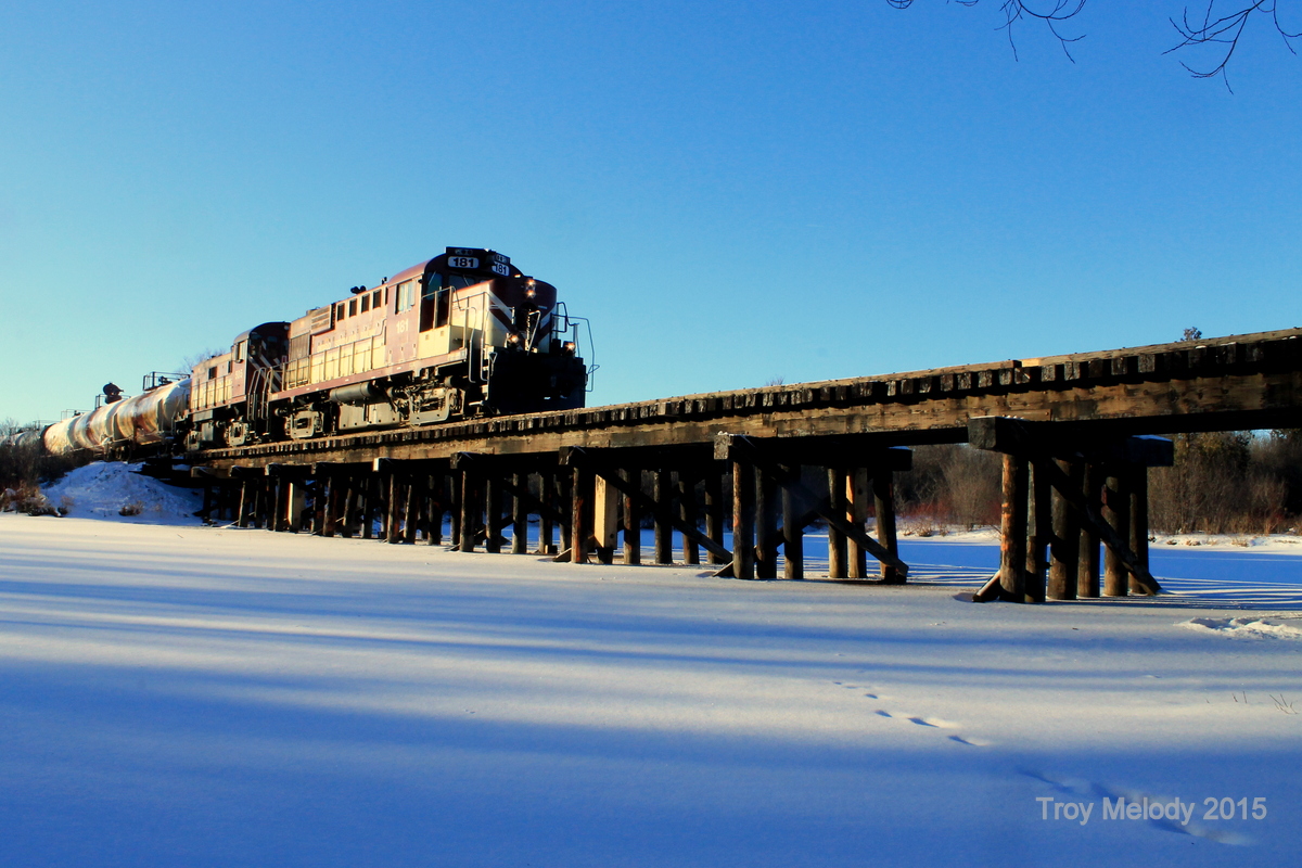 Ontario Southland RS 18u 181 pulls away from the PDI Bulk chemicals plant with a string of empty tank cars and hoppers, heading back to Guelph Jct. after a day of switching. 

It appears that the wooden bridge crossing the Eramosa river is up for repair, since the bridge piers are marked with orange markings indicating sections requiring replacement.