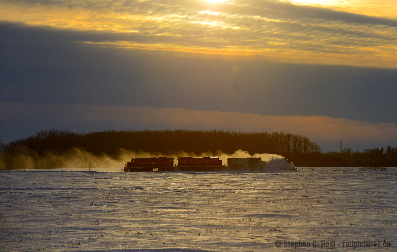 In the wake of snow kicked up by the plow, a trio of geeps are seen as a silhouette. The battle against mother nature never really ends up in Stratford, not until temperatures rise above zero in the Spring. In deference to mother natures strong will, GEXR crews head into the sunset with 6750 horsepower and  a plow, destination Goderich.