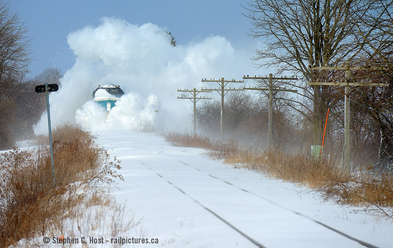 VIA steals the show in the Snowbelt...
It's been 5 hours since the last passenger train, and mother nature is angry. It's cold, -15C, the prevailing winds are blowing from Lake Huron at about a continuous 40 KM/H and as a result the snow on the ground drifts. Boy does she drift - what you see accumulated on the track is 3-4 foot high, 1500 foot long drifts of just snow. Five hours? Imagine what happens overnight! That's why we have plows on GEXR and OSR in Ontario. Formula for plowing on Ontario: Viscous (non frozen solid) Snow on the ground + Continuous wind (30+ kph sustained for hours at a time) and no train for a while = Snowplows. Or in this case, you do have VIA.. 

In the distance I hear the continuous, muffled sound of a familiar horn and soon you see puffs of white stuff appear down the track, growing ever closer. For brief moments, and I mean really brief moments, the nose of a VIA locomotive peeks through the plume - enter Evidence A above. The vast majority of photographing a VIA train plowing through a long cut of drifted snow is just a plume of white. Why though? 6437 lacks blades and wings like those on a snowplow which would effortlessly throw snow in either direction, by which, the crew would (mostly) retain visibility in the high plow cab. :) VIA engineers see nothing but white, the horn is left on continuously or you'd plug it up and render it useless, plus you do have a crossing coming up Believe it or not GEXR 518 followed this train.. with a snowplow extra but VIA clearly stole the show.