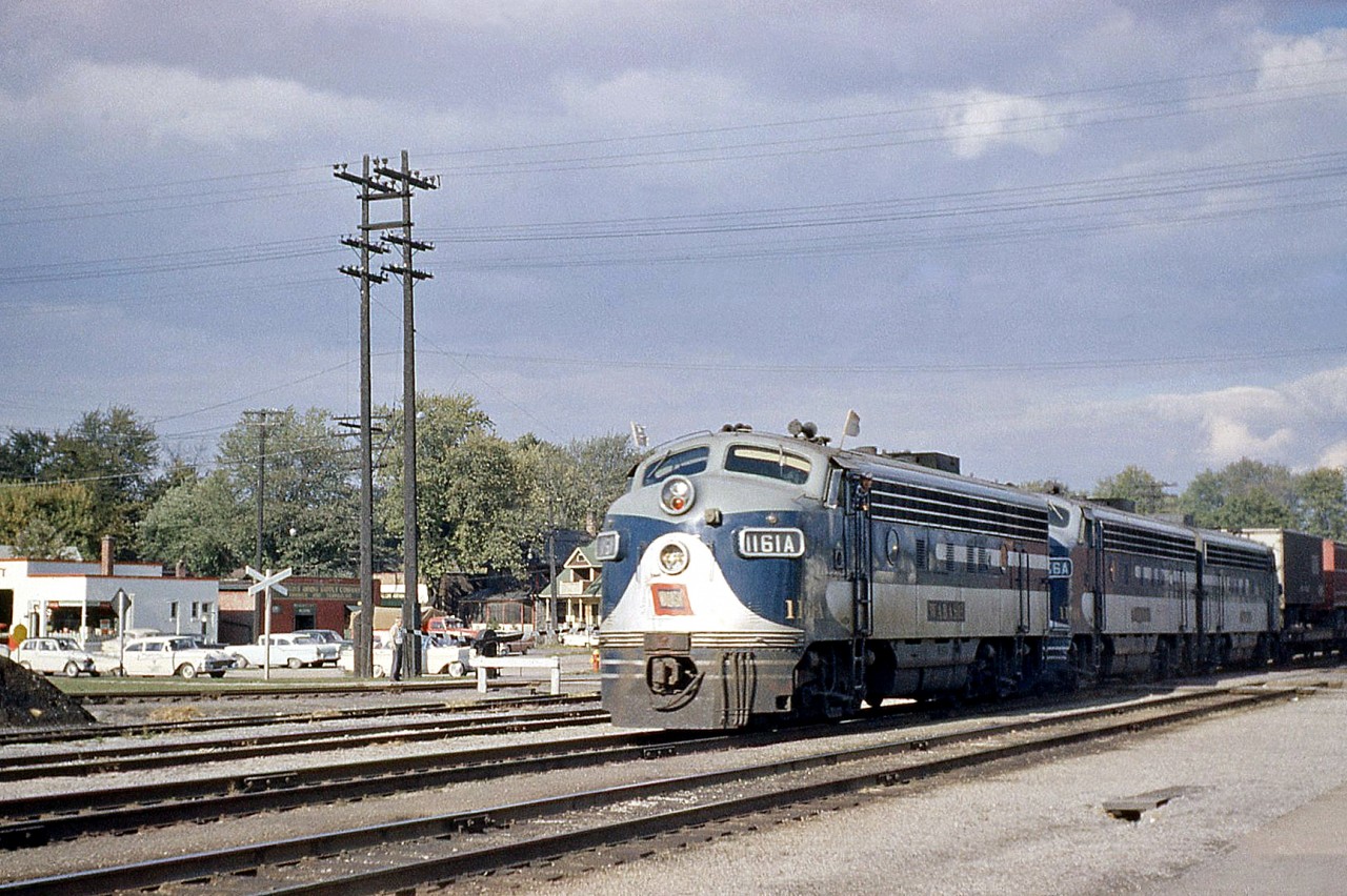 Wabash F7A 1161A leads two matching sisters on a freight through Chatham ON, on a sunny day back in October 1960. White flags waving in the wind (likely making this an extra), the train is heading westbound over Canadian National's Chatham Subdivision, crossing Queen Street by the CN station as cars line up waiting for the train to pass.  Part of an early 1951 order by Wabash to GMD London for 20 F7A's, 3 SW8's and a GP7 for their Canadian operations, interesting features on the 1161A include MARS lights in the top light assembly, silver outlined numberboard housings, the rounder passenger style pilots, and the square-topped winterization hatches found on some early GMD units. The Canadian Wabash F-unit fleet would later be renumbered into the 600-700 series, and when N&W absorbed the Wabash they became 3600-3700 series units. Leader 1161A would become WAB 670, and then N&W 3670.  For more Wabash F's: F7A's 676 and 725 meet at Fort Erie ON in Summer 1964.