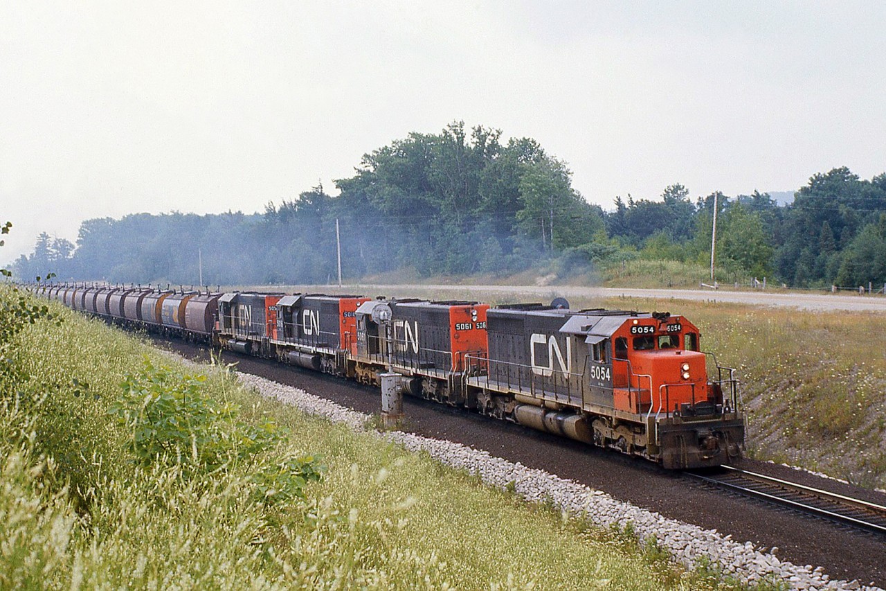 Four matching CN SD40's put their combined 12,000 horsepower to work, splitting the signals at "Mile 30" north of Milton as they motor upgrade with a dedicated unit ore train in Northern Ontario-Hamilton service.  These "shorty" cylindrical ore hoppers were built by National Steel Car for ore unit train service in three batches: 1967 and 1973/1975. The 1967 cars were 2000 cuft units assigned to Temagami ON and used in unit train service between northern Ontario and Hamilton. The later orders were slightly larger 2300 cuft cars for operation out of Bruce Lake. The hoppers were all designed for automatic loading and unloading, with wheels on the roof hatches that contacted rubbing rails to open and close roof hatches for loading, as well as automated or manual unloading capabilities. CN and Ontario Northland both bought batches and pooled them together for ore train operations (note the ONR's blue & yellow paint and chevrons on the 2nd and 3rd cars).