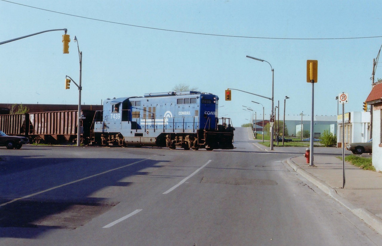 Some years ago, when Conrail (and before that, New York Central) has some presence in Niagara Falls, they ran transfers from Fort Erie/Welland over to the CN yard by way of the Niagara Industrial Lead, a line thru town that became history once the mainline thru the city's tourist area was removed. Here we see Conrail 7439 with a cut of hoppers crossing smack dab in the middle of the Bridge St/Victoria Av intersection in the Falls. Just in behind on the right one can see the elevated roadway over the CN Grimsby Sub. Such localized activity has all but vanished in the Falls, as it has in most railroad communities.