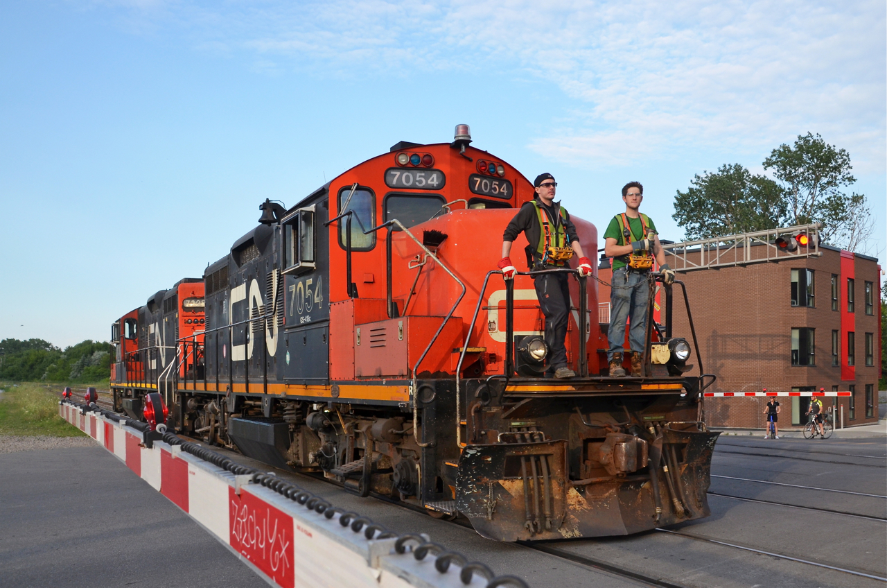 Two GP9's, two crewmembers and two beltpacks. The Pointe St-Charles switcher heads west light through the St-Henri neighbourhood of Montreal with a pair of GP9's (CN 7054 & CN 7228) about 80 minutes before sunset. Two crewmembers are on the front of the lead engine and both have beltpacks.