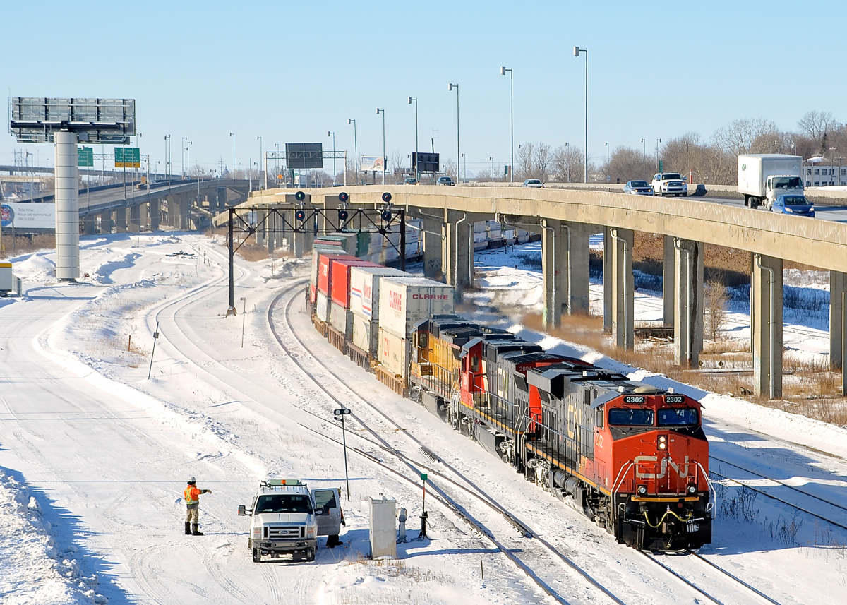 CN 120 with CN 2302 leading two ex-UP C40-8's (repainted CN 2004 and yellow CN 2001) heads east through Turcot West in Montreal. It is passing some MoW personnel who are at the switch for the Lachine spur (at left).
