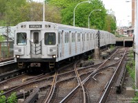 A train of now retired UTDC/Can Car Rail H6 subway cars heads west to Keele Subway Station in one of the open cuts along the line, passing crossovers that were once used everyday when the Bloor-Danforth line only went as far as Keele. In the background buses can be seen at the nearby Dundas West station, from where this train has just departed. The switch on the right leads to Vincent Yard, a small storage yard between the two stations.