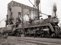 After one of the last CN steam excursions to Fort Erie, CN 6060 is serviced before returning to the roundhouse.  A shopworker climbs on top of the boiler to fill the sand dome.  The old coaling tower looms over the servicing tracks, although it hasn't been used for years.