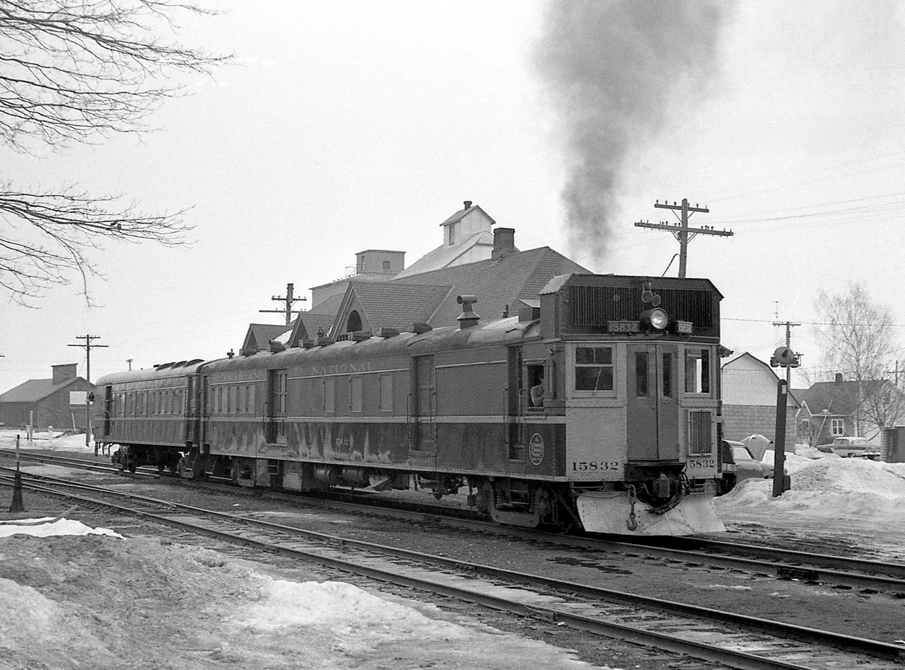 Canadian National "doodlebug" 15832 with a combine trailer in tow throttles up at the station in Stayner ON, enroute to Meaford.  Oil-Electric 15832 was built in 1930 by Canadian Car & Foundry, a self-propelled passenger car often known as a "doodlebug". Popular for use on branchlines or lines with low passenger ridership in the steam era, they were precursors to the widely successful Budd Rail Diesel Car (RDC) of the 50's. This car is painted in a variation of CN's typical yellow and green 1954 scheme, with a yellow front end and plow but with red front doors.  Stayner was Mile 22.8 on CN's Meaford Sub, which ran from the Bala Sub at Barrie 52.2 miles to Meaford.  More on the Meaford Sub: CNR 1322 at Meaford, 1958: http://www.railpictures.ca/?attachment_id=14023 CNR 1527 leaving Meaford in March 1958: http://www.railpictures.ca/?attachment_id=15383