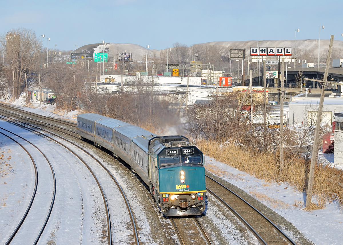 VIA 69 has left the island of Montreal but is already 25 minutes late due to a late departure from Central Station. Here it passes through Montreal West with VIA 6440 leading. In the background are mountains of snow collected by the city.
