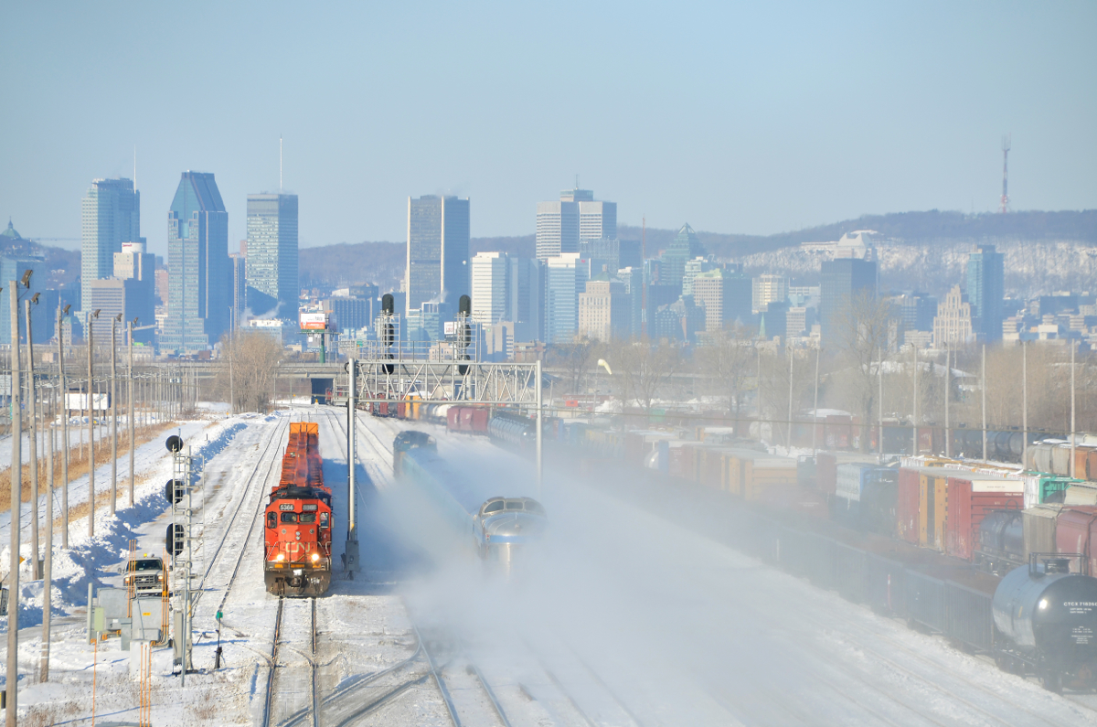 A Park Car passing an SD40-2. VIA 15 from Halifax (The Ocean) is passing through Southwark Yard in St-Lambert, Qc, passing a stopped rail train (CN 905) which has CN 5366 in the lead. Soon VIA 15 will be in downtown Montreal, whose skyline can be seen in the background. Bringing up the rear of VIA 15 is an unidentified Park car.