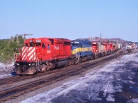 From a personal standpoint I cannot believe it has been 18 years since I took this picture. Or worse, that long since I spent a fair amount of time foraging around this area. Time goes so fast !!! It is April, but there is still snow hanging around; I remember that year there was one heck of a lot of it.  I am standing on a snowbank at the south end of the community where excess snow was piled up. This Grain Train from the west is powered by CP 5951, HLCX 6211, SOO 769, CP 5648, and CP 752. I will note locomotives in this consist now retired, as the CTG shows the leader only one still active. (don't know about the HLCX)  The preserved station is barely visible at the curve in the distant background; Cartier yard can be seen on the right. Also out of sight on the right is 90% of the community, connected to the rest of the world solely by Spencer Av crossing; of which the first revenue car in the train is rolling over in the photo.