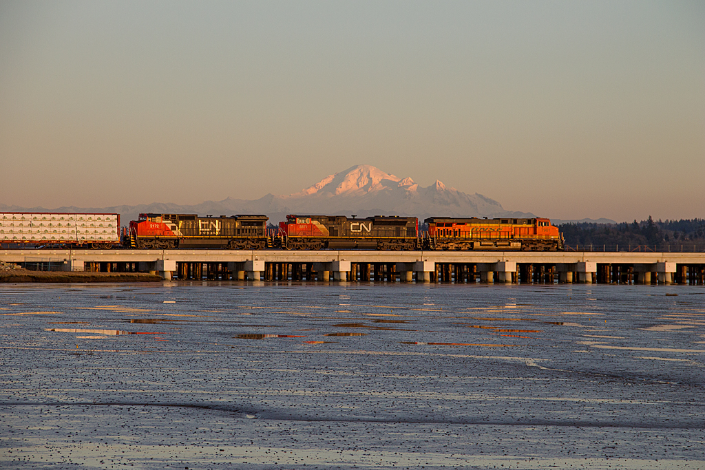 On a nice, sunny Sunday evening southbound VBCEVE (New Westminster, BC - Everett, Wa) crosses the newly decked portion of the Mud Bay trestle, with Mount Baker being highlighted by the evening light. The trestle, which was originally wooden, has fallen victim for the need to be upgraded as an increase of heavier BNSF coal traffic has become more frequent to Roberts Bank Coal Port.