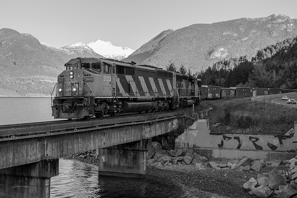 The daily CN Squamish Switcher is seen passing along the Howe Sound of the Sea to Sky highway, passing the historic mining town of Britannia, BC. On this morning CN SD60F 5523 and two other EMD work horses are tasked with hauling this train, which is returning southbound back to North Vancouver. 

Its turning out to be a nice day, however by the time the train came along, the sun hadnt quite reached around to our chosen spot, thus the black and white treatment, which Im quite happy with.