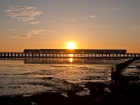 The setting sun works its way down the horizon, as Amtraks Cascades 517 heads south for Seattle from Vancouver. The train is crossing the Mud Bay trestle, which has recently undergone a re-decking from a wood to concrete. 