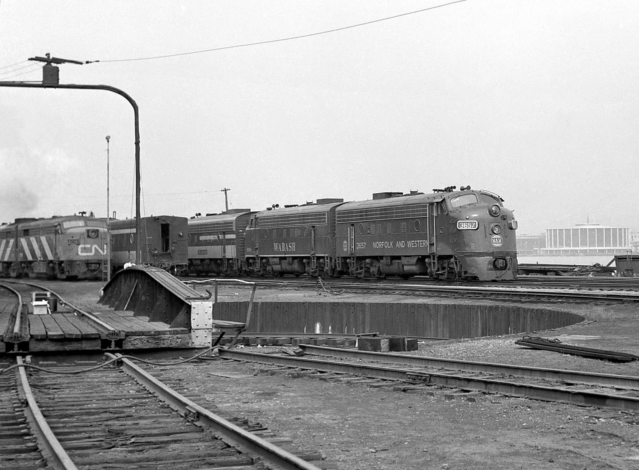 Different power and different paint schemes: resting near the roundhouse turntable at the Canadian National shop facilities in Windsor ON is a set of Norfolk and Western F-units, built for the Wabash Railroads' Canadian operations. By this time the Wabash Railroad was leased to the Norfolk and Western (before they took control in 1970 from majority owner PRR) and some power was already repainted. Witness F7A 3657 (ex-Wabash 657, originally 1155 and the first GMD-built Wabash F-unit) sporting the N&W livery, while the sister unit behind sports the later simplified Wabash livery, and the 3rd F is in its original as-delivered 1100 series paint scheme. N&W renumbered the Wabash F's by adding a 3 to the start of the road number (or if you prefer, adding 3000 to it).   On the left is a set of CN power with an MLW FPA-unit on point (possibly 6758) and a steam generator car on the next track, both used on Windsor-Toronto-Montreal corridor passenger trains. On the right across the river is the motor city: Detroit, home of General Motors, parent company of Electro Motive Division who designed F-units like 3657 and her kin.  More Wabash/N&W Canadian F's: Wabash 1161A at Chatham, 1960: http://www.railpictures.ca/?attachment_id=17612 Wabash 726 at Simcoe station in 1964: http://www.railpictures.ca/?attachment_id=18211 Wabash 676 & 725 at Fort Erie in 1964: http://www.railpictures.ca/?attachment_id=15707 N&W 3726 and 3666 at Thamesville in 1974: http://www.railpictures.ca/?attachment_id=18006 ...and... More modern power at Windsor Roundhouse in 1985:http://www.railpictures.ca/?attachment_id=16464