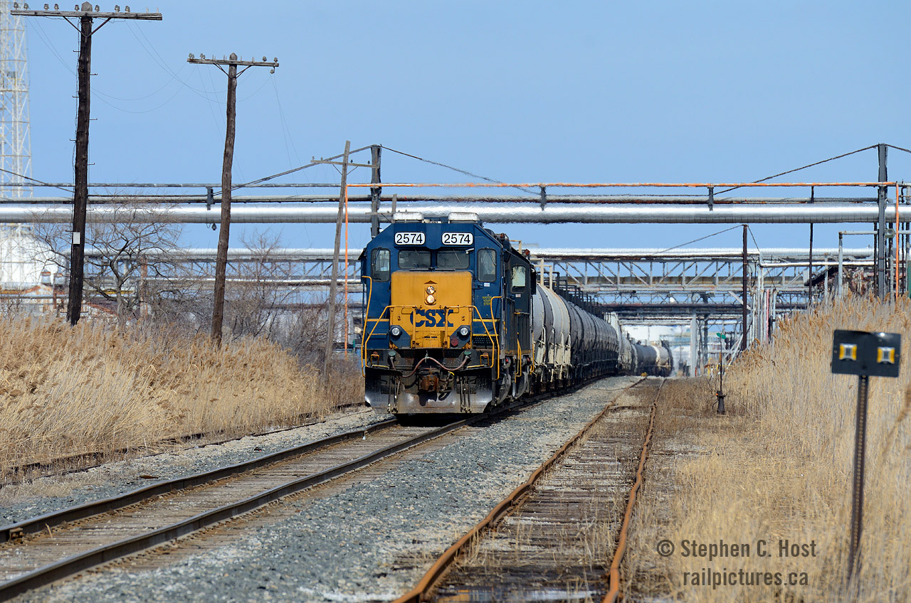 At Sarnia - CSXT Y120 is framed in a canopy of pipelines that join adjacent refineries and chemical plants, whom also depend on the railways service to stay active.

The crew of Y120 is nearly done for the day, and is seen shoving their 80 car train into Sarnia Yard. Once done, the crew will cut off from their engine and caboose and return to the Clifford St Pere Marquette depot and Erie and Huron built roundhouse light engine. 

I could be wrong, but it appears the flanger sign at right is illuminated or reflective... anyone have info on this?