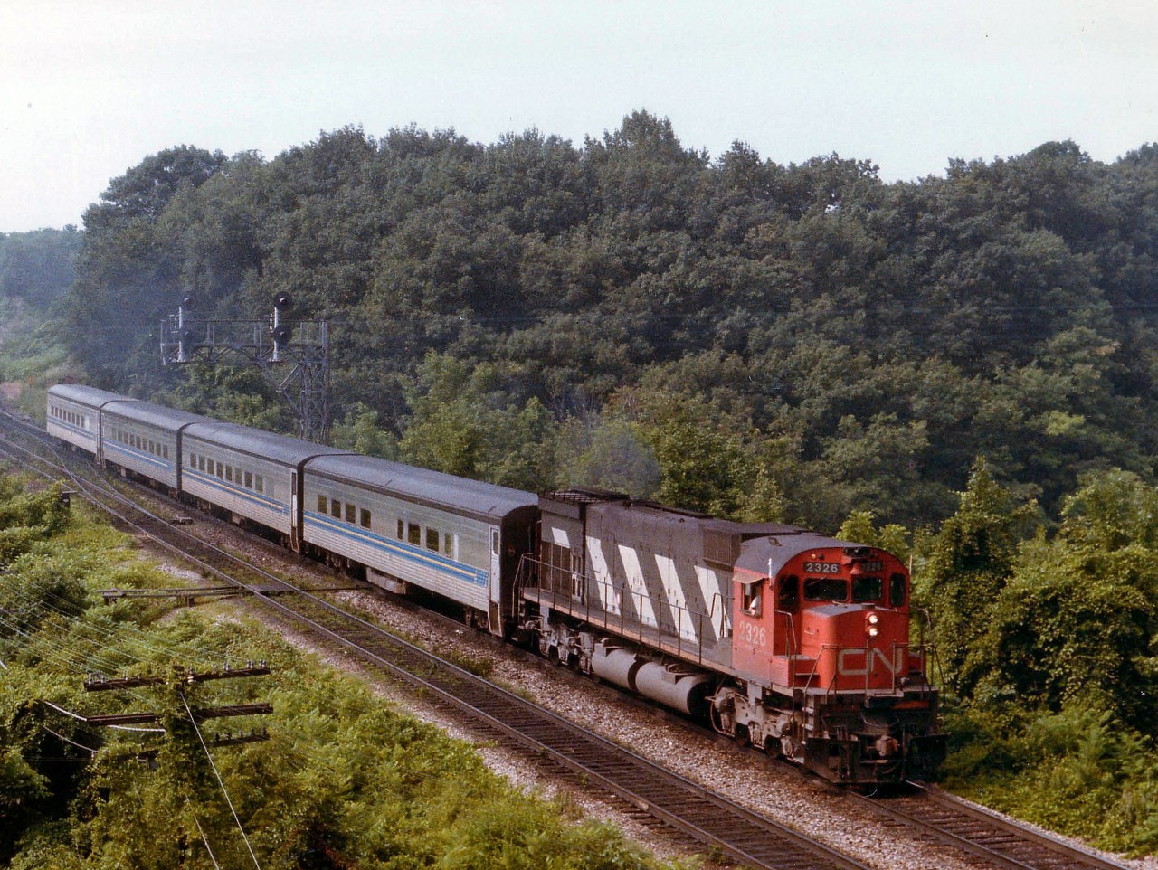 It is a steamy hot and hazy August morning and this comes down the hill at Bayview heading East. I marked it as #80, the morning VIA, but I cannot recall now whether this train  had a baggage car or not. I keep thinking it was always a 5 car train.  And the unusual leader, MLW M-636 #2326, has 'extra' flags. What gives?  Yes, we know it is extra unusual and the probable Tempo engine of the day has crapped out somewhere. One thing for sure, railfans even back then no doubt would pay a tad extra to ride behind this behemoth just to listen to her work.  Unit was retired by 1996.