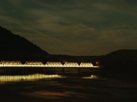 Under a starry sky, the headlight of the westbound Ocean illuminates the rail bridge over the Ristigouche River as it slows for a station stop at Matapédia. The shore to the left is New Brunswick, to the right is Québec.
