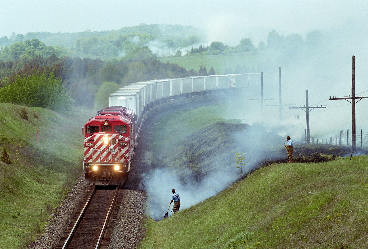There used to be a pair of handsome old wood road bridges crossing over the adjacent CN and CP tracks on Nichols Road, Newtonville, about 50 miles east of Toronto.  In June of 2001 an eastbound CP train of piggyback flats rolls slowly past the local fire department trying to put out trackside fires, likely caused by an earlier train.  The lead unit, CP 9024, is an EMD SD40-2F, a locomotive that was unique to CP Rail.