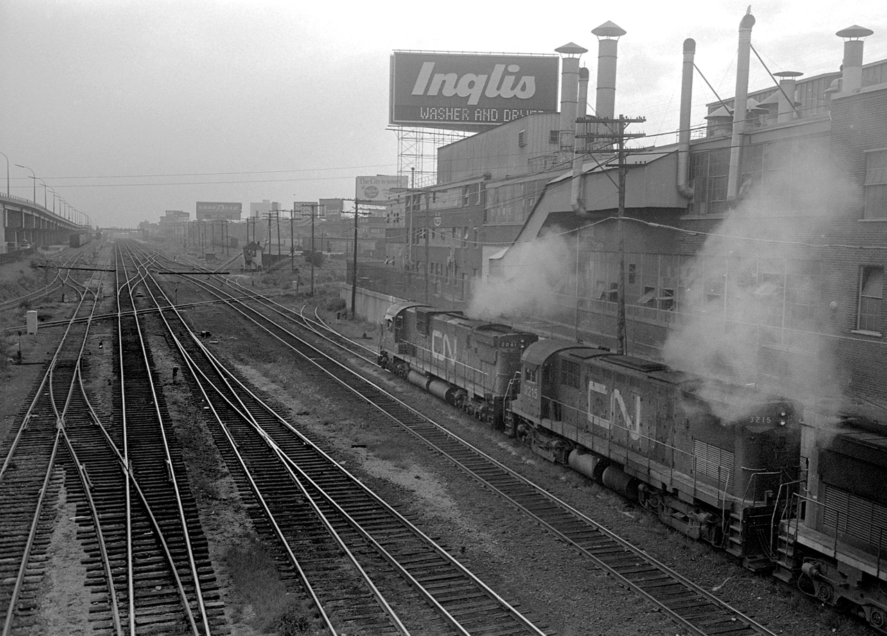 On a murky evening in 1978, a CN freight train with MLW power heads west past Fort York in this view from Strachan Avenue.  The train is about to cross the Wharf Lead that led south from Parkdale to the waterfront, originally the old Toronto, Grey & Bruce Ry. narrow gauge mainline to the Queens Wharf.  On the north side of the tracks is the old Inglis plant, on the left is the CNE siding.