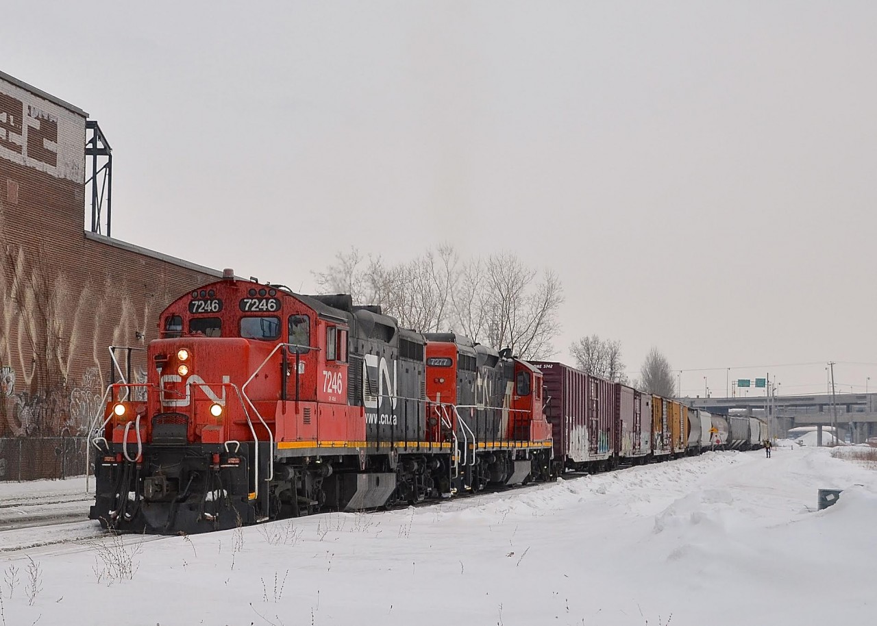 CN X527 has a pair of GP9's (CN 7246 & CN 7277) as it heads back to Pointe St-Charles yard with a long string of cars being pulled from the Turcot holding track in the St-Henri neighbourhood of Montreal. The brakeman in the distance will have to take a taxi back to the yard; the train is so long that it will stall if they stop long enough to let him climb aboard the power.