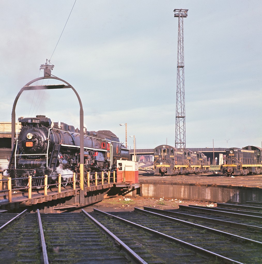 It looks like the late Del Rosamond got up early to catch #6167 before she headed over to Union Station for her next fan trip. As the sun rises, her white-painted driver wheels and full load of coal made for a regal scene. Built in 1940 by MLW, she served her last excursion on September 27th, 1964. Meanwhile, a gaggle of S2 and S4 diesels wait for servicing and their next assignment.