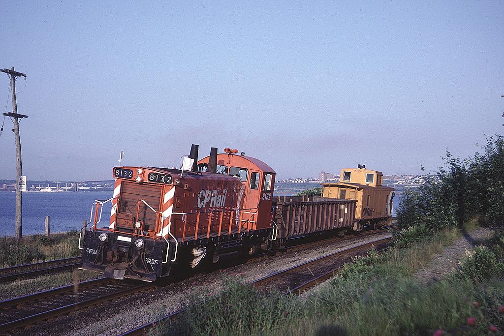 In 1981 Dominion Atlantic Railway did its interchange with CN in Rockingham Yard and could be counted on to show up almost every evening (Monday - Friday) with at least a couple of cars. SW1200RS has swapped cars with CN and is heading west for home rails at Windsor Jct with a single CN gondola. The train is at the west end of Rockingham Yard, running along the shore of the Bedford Basin. The McKay bridge between Dartmouth and Halifax can be seen in the background.