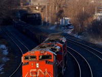 <b>Darkness and light.</b> As Montreal West is built on on an escarpment, it can get shadowy at track level on CN's Montreal sub well before the sun sets. Here the nose of CN 8899 is the only thing well lit at track level as CN X321 heads west about 45 minutes before sunset earlier this evening. The lashup is 4 GMD units (CN 8899, CN 8936, CN 5551 & CN 4724). 