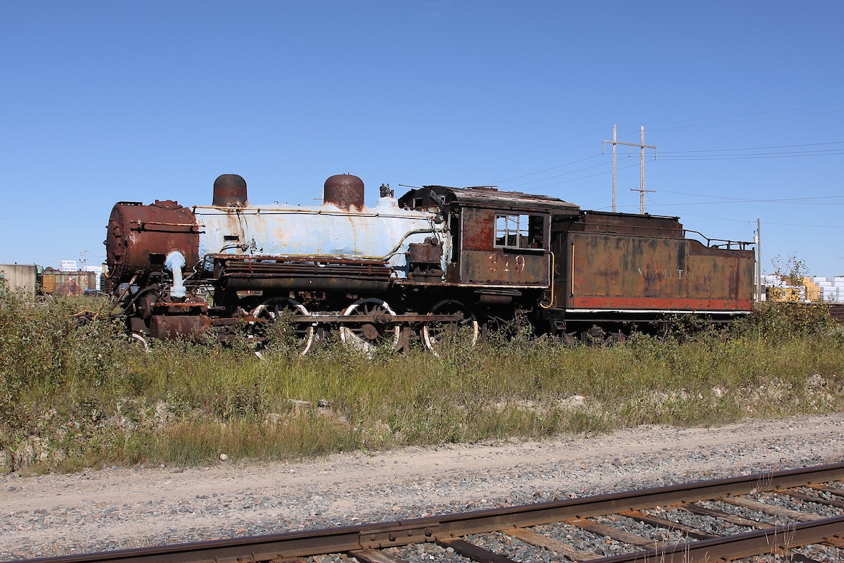 219, a 4-6-0 locomotive built by MLW in 1907, sits in Cochrane Yard surrounded by years of plant growth.   She was originally numbered 119 for the Temiskaming and Northern Ontario Railway, renumbered in 1935 and then sold to Normetal in 1938.  Ontario Northland required her in 1975 for a planned excursion train that never did materialize.  The Northern Ontario Railroad Museum and Heritage Centre bought her in the summer of 2012 for the sum of $5001, and was eventually transported to their facility at Capreol in the spring of 2014.  When I stumbled across her she was clad in a coat of sealant (to prevent aspestos from leaking into the environment) as well as missing a smoke stack (which has since been reattached).