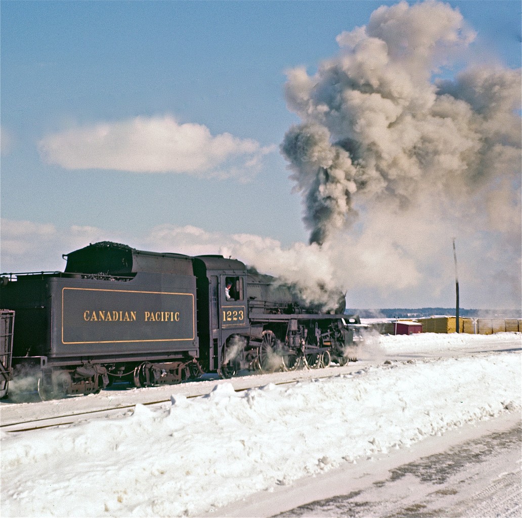 It looks like a chilly winter's day in Pembroke - the polar opposite to last week's Rosamond upload here on RPca.  


The engineer is seen in this image looking directly at Del - perhaps wondering why he is taking pictures of an old steam locomotive.  The location is the lumber yard of the Consolidated Paper Corporation.   It was immediately across the tracks from the CPR stone station.  The satellite image now shows just a few town-homes and some open fields.


The water tower which held the supply for the local steam trains is still in use today.  It sits at the corner of John Street and Nelson Street.  On the side of this tower is a huge mural featuring the long-gone station and this very locomotive, #1223.  


Del's sister, Gloria, tells me that the interior of the station featured beautiful wood.  Before the station was finally torn down, the wood was purchased by a local school teacher and used in her Quebec cottage.
