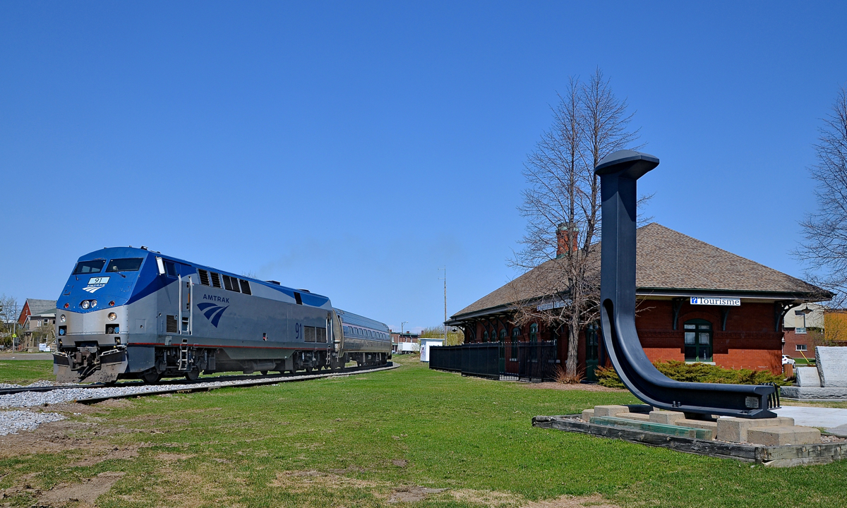Past the St-Jean station and the spike. The southbound Adirondack is rounding the curve in front of the ex-Grand Trunk station in St-Jean-sur-Richelieu. At right is an oversized spike to commemorate how this was the terminus of Canada's first railway.