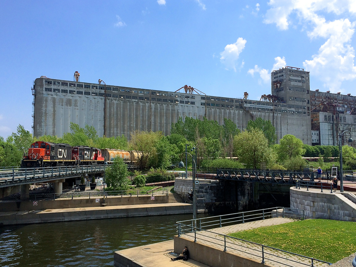 CN 7015 & CN 7246 are inbound into the Port of Montreal as they cross the Lachine canal. Behind them is the massive Grain elevator #5, out of use for about twenty years now. The first section of the elevator was built by the Grand Trunk Railway.